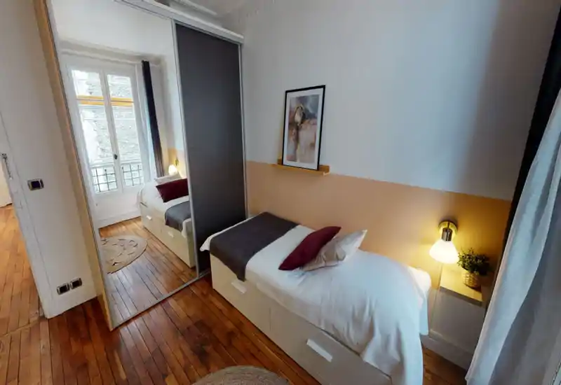 Camera singola luminosa e accogliente con letto ben rifatto, lampada da comodino calda e armadio con specchio che amplifica lo spazio.