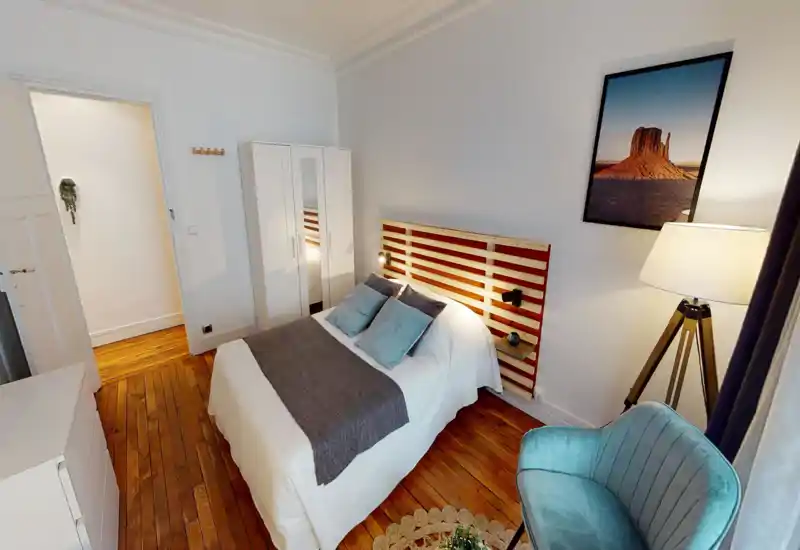 Bright, stylish bedroom with a double bed, wooden slatted headboard, wardrobe and cozy seating. Warm wooden floor and soft textiles create a welcoming atmosphere ideal for rental listings.