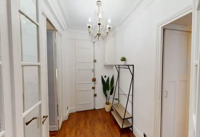 Bright, elegant entry hallway with a chandelier, wooden floor and a slender coat/bench rack — a welcoming transitional space.