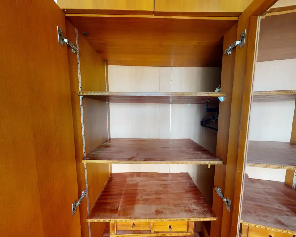 Interior of a wooden wardrobe/closet with multiple shelves and a small set of drawers; suitable to show storage space in a listing.