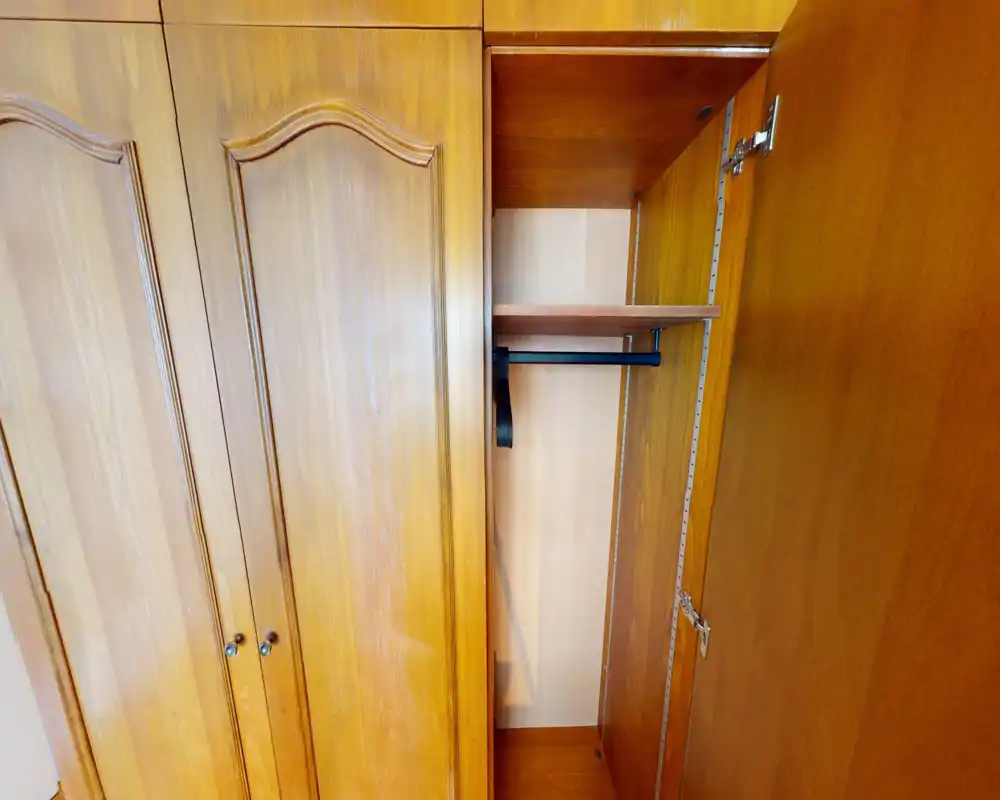 Wooden built-in wardrobe with open door showing an empty hanging rail and shelf — clear close-up useful for storage detail in a listing.