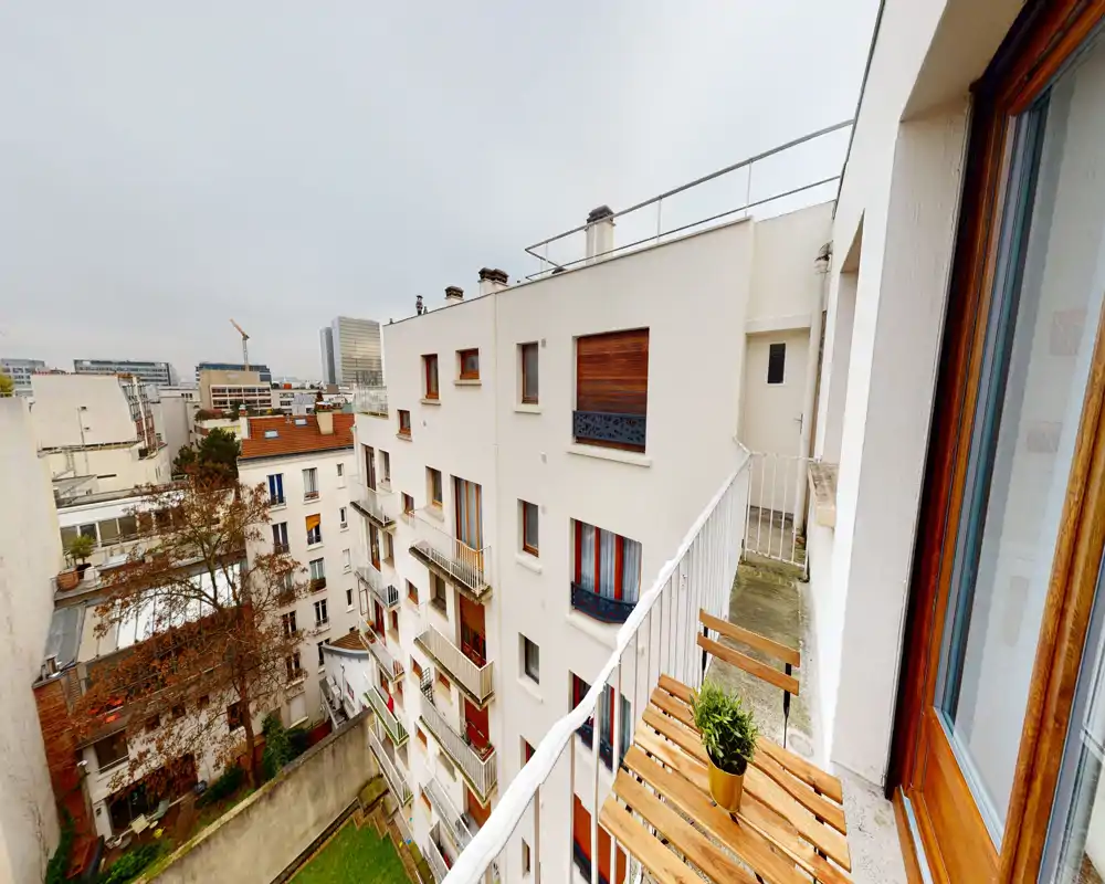 Sunny-feel city balcony with a small wooden bistro table and chair overlooking neighboring buildings — ideal for morning coffee and urban views.