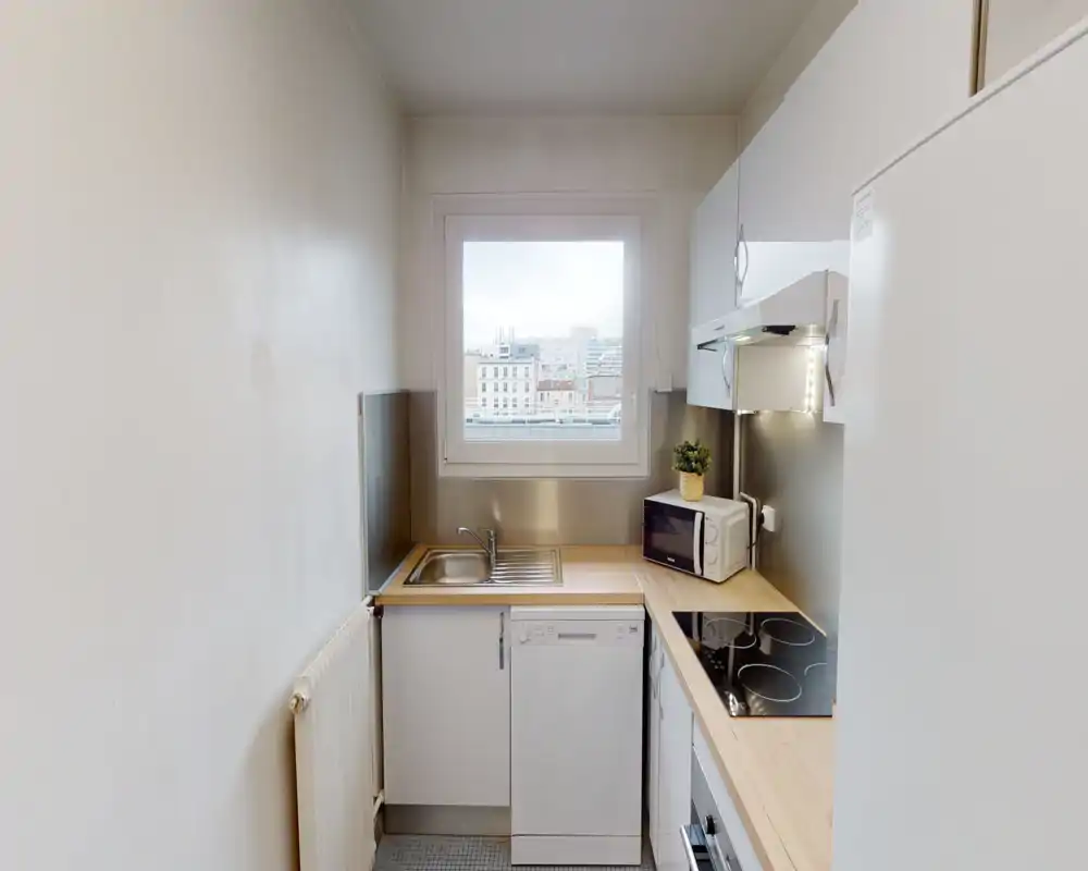 Compact, modern kitchen with a windowed view, stainless sink, ceramic hob and integrated appliances. Light wooden countertops and white cabinetry create a clean, practical cooking space ideal for a city apartment.