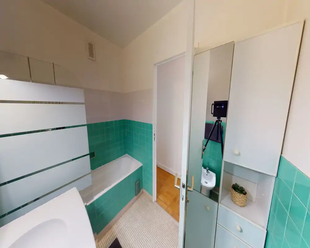 Small vintage bathroom with turquoise wall tiles, bathtub, sink and mirrored storage cabinet; bright, clean and compact space ideal for short-term rentals.