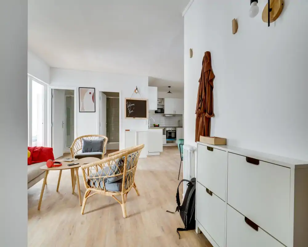 Bright, modern living area with rattan armchairs, a small coffee table and a sofa by the window — an airy, well-styled space ideal for relaxing.