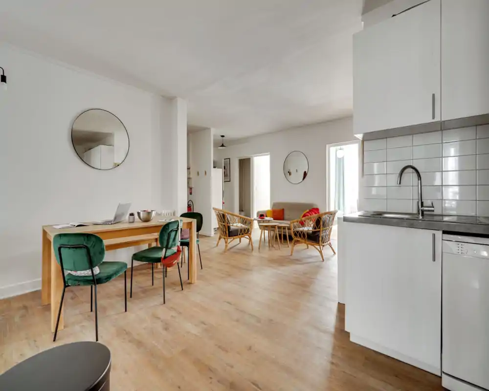 Bright open living area with a small lounge set, dining table and visible kitchenette—modern, airy and furnished for comfortable socialising.
