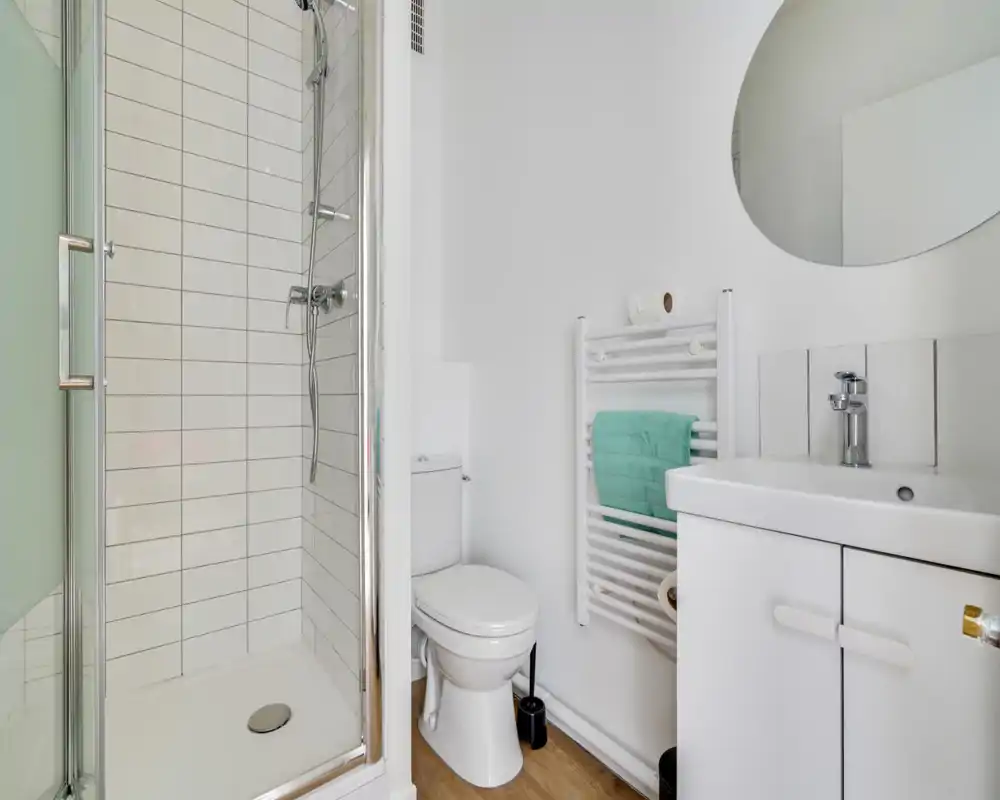 Bright, modern bathroom with a glass shower cubicle, white tiles, wall-mounted towel radiator and a compact sink cabinet.