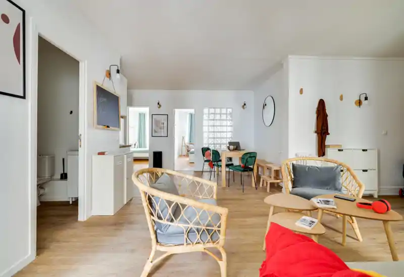 Bright, stylish open living area with rattan seating, a small coffee table and a dining nook in the background. Natural light and warm wood floors create a welcoming, modern atmosphere.
