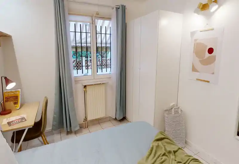 Bright, compact bedroom with a double bed, wardrobe and a small desk by the window. Soft blue textiles and minimalist decor create a calm, inviting feel.