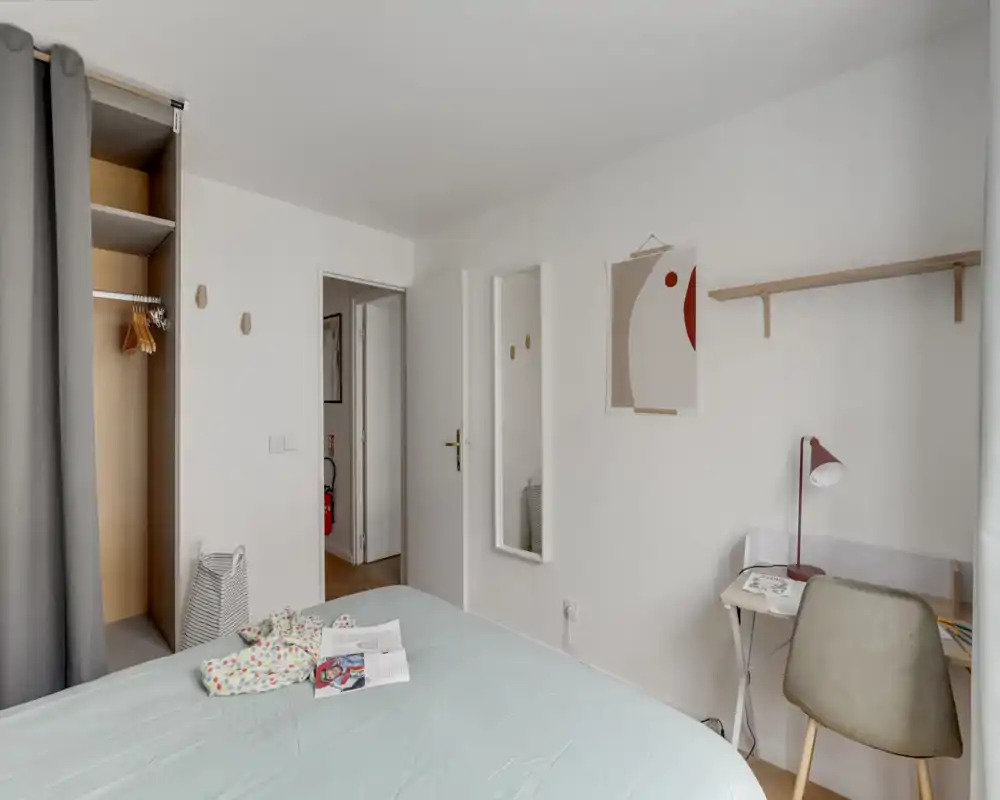 Chambre lumineuse et minimaliste avec lit bien visible, petit bureau et étagère ; tons neutres et textiles doux pour une ambiance calme et moderne.