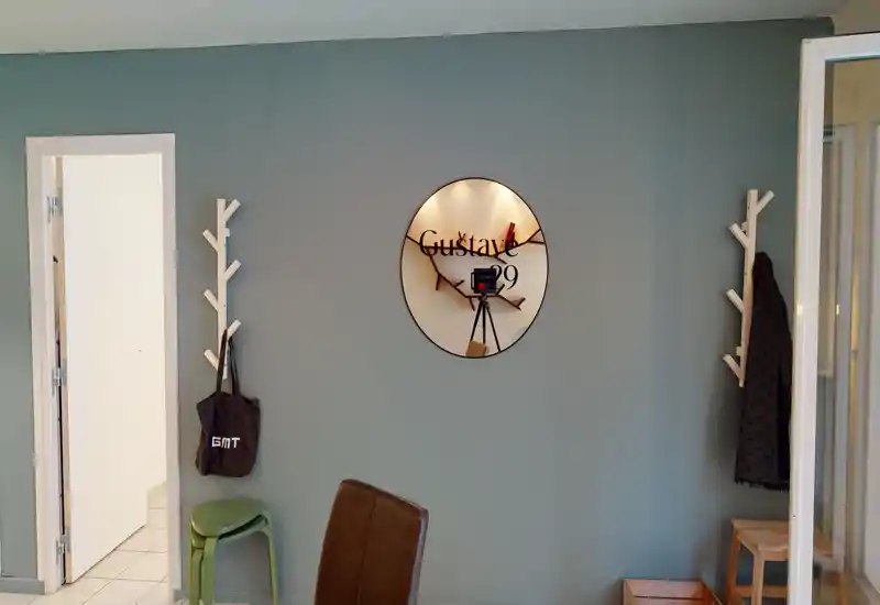 Simple living area with a muted green feature wall, decorative round mirror, wall hooks and seating — neat, functional and well-lit space suitable for an entry or small lounge.