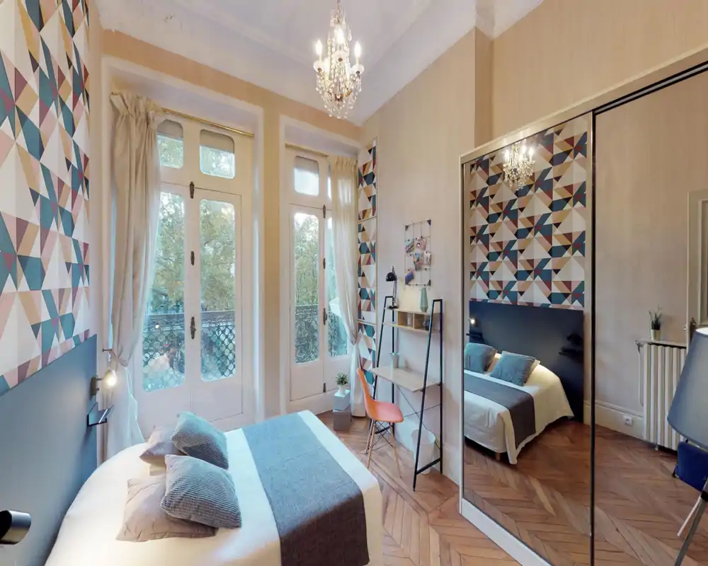 Bright, stylish bedroom with a double bed in the foreground, geometric accent wall, large windows and a mirrored wardrobe adding depth.