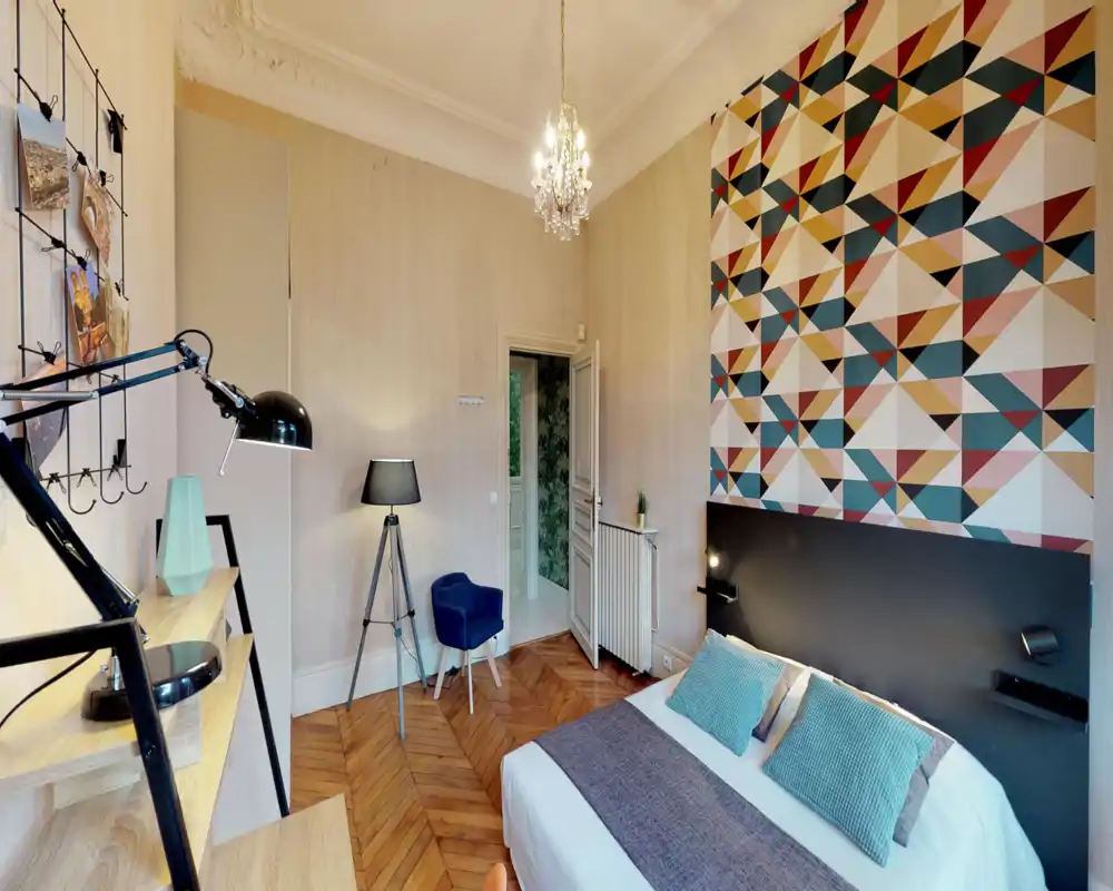 Bright, stylish bedroom with a double bed, patterned accent wall and wooden herringbone floor. The room features modern lamps, cushions and tasteful decor creating a cozy atmosphere.
