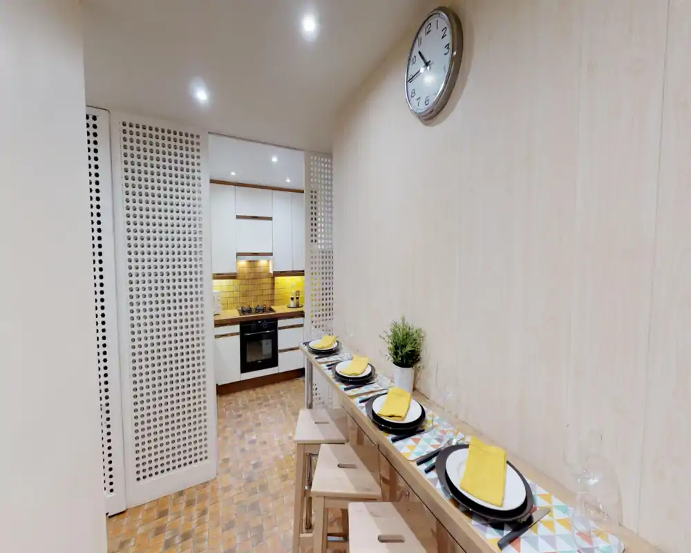 Compact open kitchen with a narrow breakfast bar set for four; warm yellow backsplash tiles, wooden stools and under-cabinet lighting create a cozy, well-styled kitchenette.