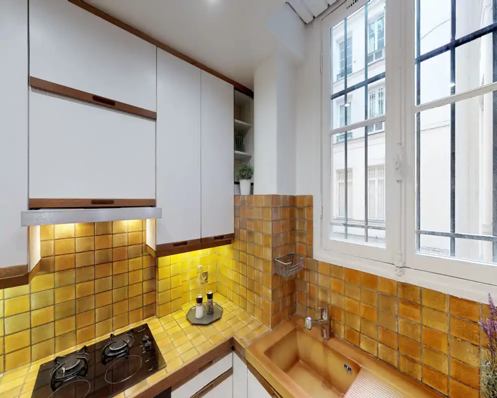 Bright, compact kitchen with warm ochre tiles, built-in stovetop and a deep sink by the window — ideal for cozy city apartments.