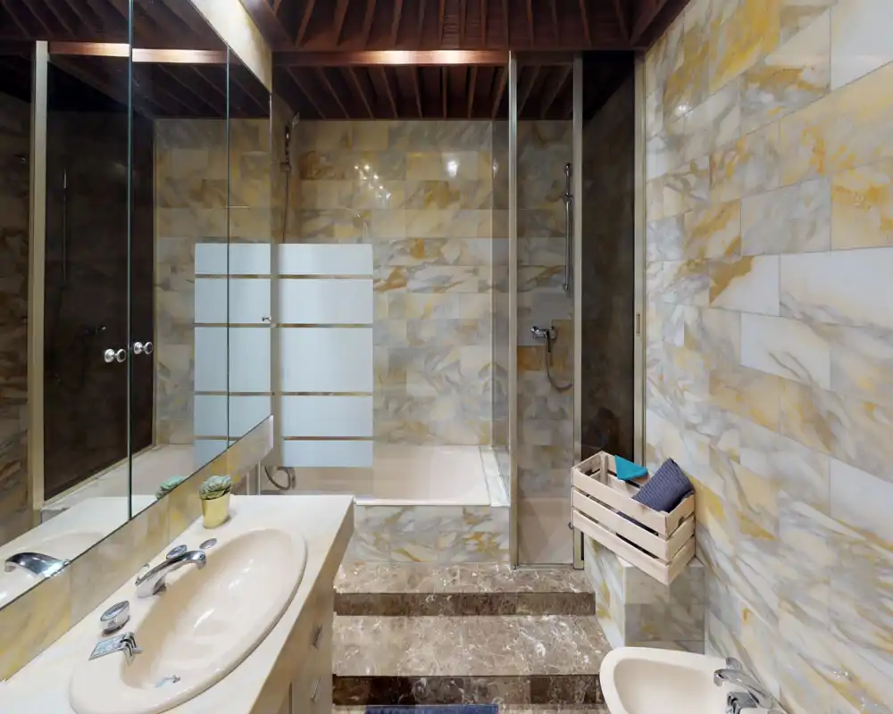 Contemporary marble-tiled bathroom with a glass-enclosed shower, built-in bathtub, and vanity sink. Warm wood ceiling and decorative crate add a cozy touch.