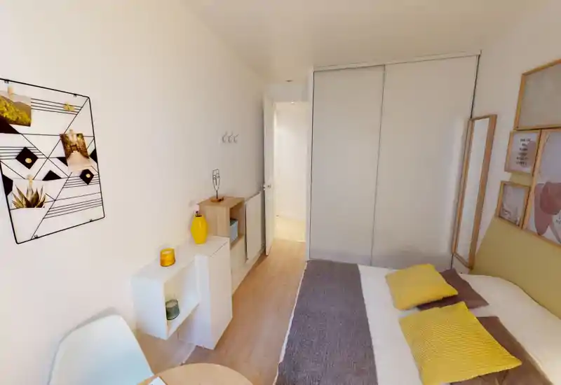 Chambre moderne et lumineuse avec lit double décoré d'oreillers jaunes et d'un plaid gris, placard coulissant, étagères simples et décoration minimaliste — chaleureuse et soignée pour une annonce locative.