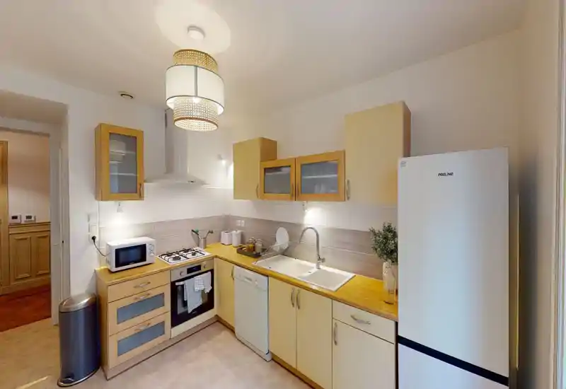 Cuisine lumineuse et bien équipée avec plan de travail en bois, four encastré, lave-vaisselle et grand réfrigérateur — propre, moderne et accueillante.