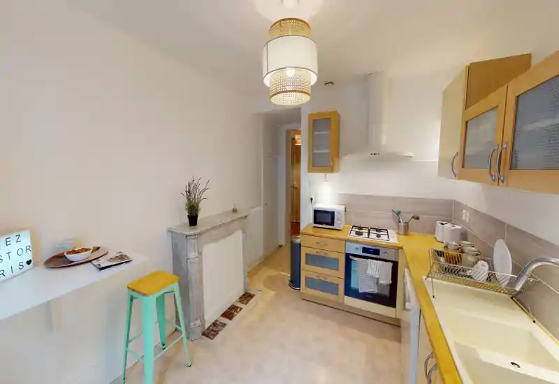 Cuisine compacte et bien équipée avec plans de travail en bois, four encastré et plaque à gaz, meubles hauts et évier ; tons chauds et décoration soignée pour une atmosphère accueillante.