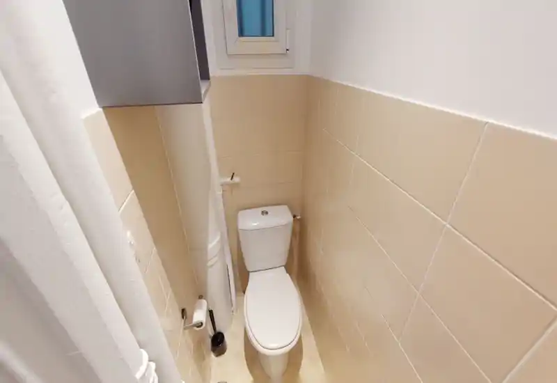 Toilettes compactes et lumineuses avec murs carrelés beige, WC et une petite fenêtre dépoli apportant ventilation et lumière naturelle.