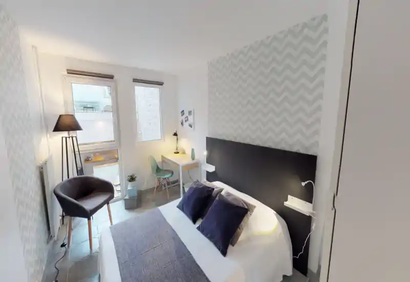 Bright, stylish bedroom with a large double bed, patterned accent wall, bedside lamps and a small workspace by the window — ideal for comfortable short stays.