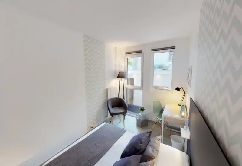 Bright, well-styled bedroom with a large bed in the foreground, cozy pillows and a bedside desk with lamp — ideal for a relaxing stay.