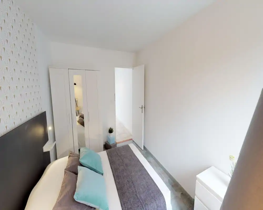 Bright, modern bedroom with a neatly made double bed, decorative pillows and a full-height wardrobe with mirrored door. Clean white walls and soft accents create a calm, welcoming space ideal for rentals.