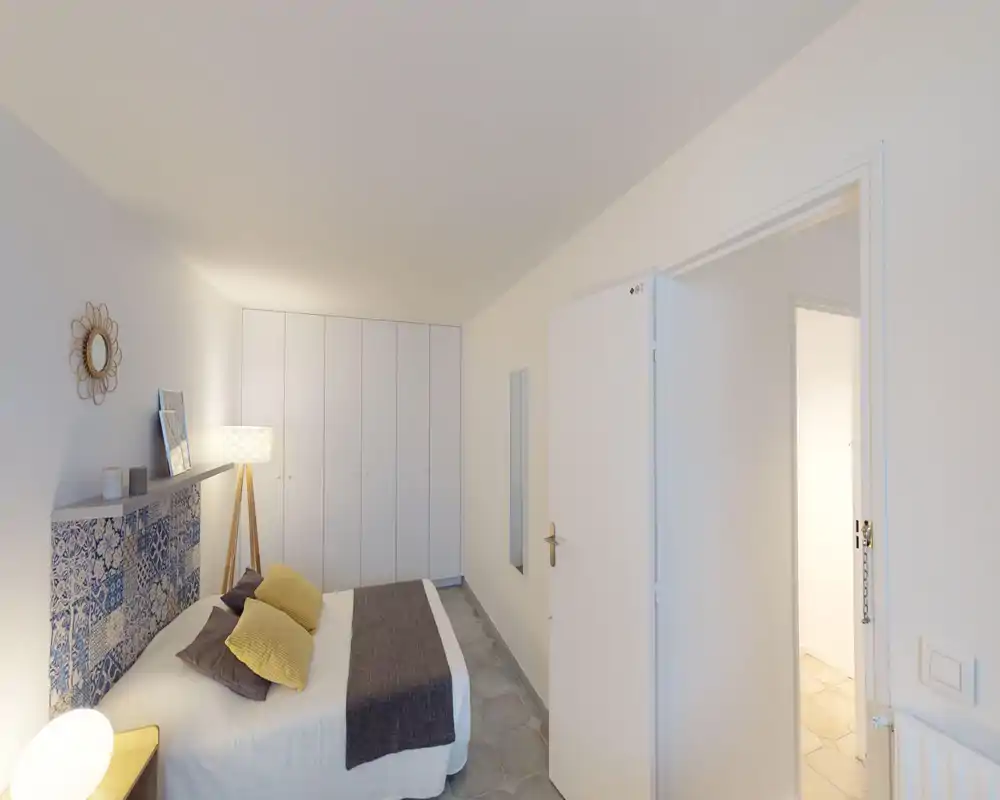 Chambre lumineuse et moderne avec tête de lit à motifs, grand placard intégré et éclairage d'appoint chaleureux. Le lit double est bien fait avec des coussins contrastés et un plaid confortable.