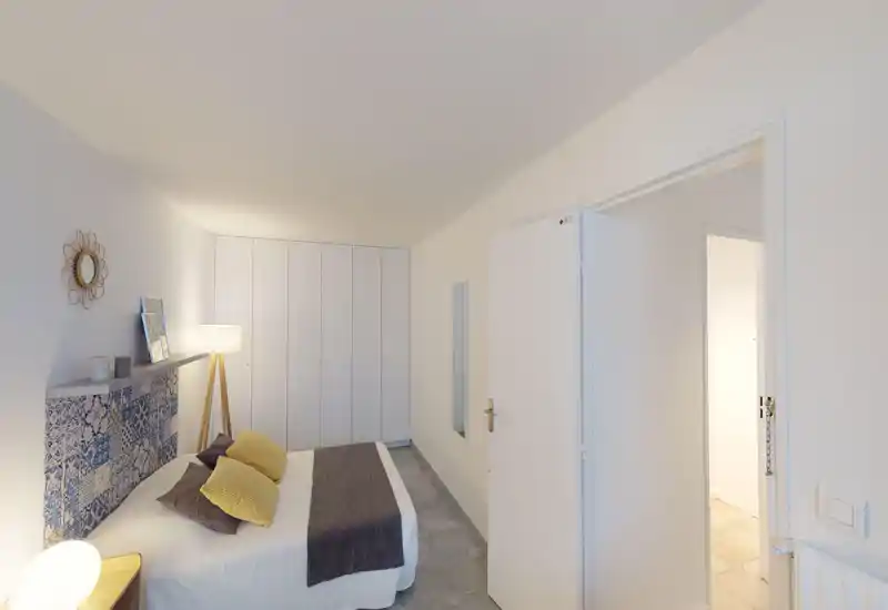 Chambre lumineuse et moderne avec tête de lit à motifs, grand placard intégré et éclairage d'appoint chaleureux. Le lit double est bien fait avec des coussins contrastés et un plaid confortable.