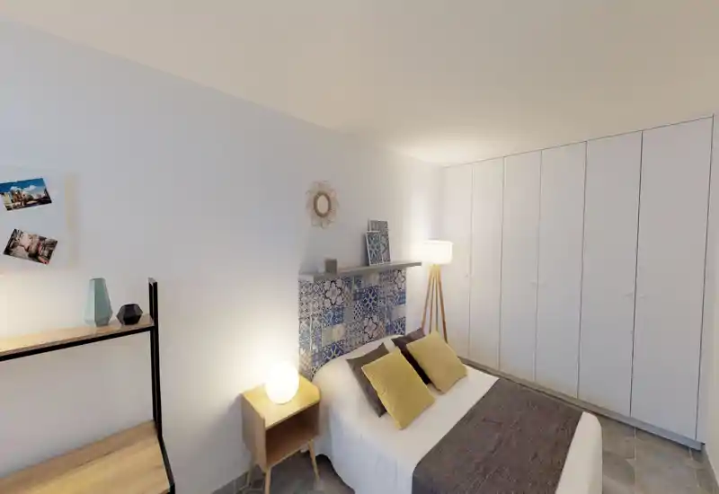 Chambre moderne et lumineuse avec lit double, tête de lit à carreaux décoratifs et placard intégré. Lampes de chevet chaleureuses et coussins décoratifs offrent une ambiance cosy, idéale pour une annonce locative.