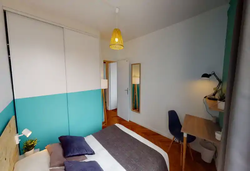 Chambre lumineuse et moderne avec lit double, textiles confortables et petit bureau; mur accent turquoise et parquet bois apportent une ambiance chaleureuse.