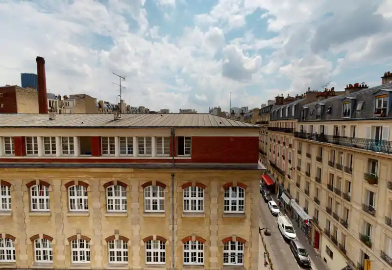 Vue sur la rue et les toits de style parisien : photo en pleine lumière montrant façades, toits et ciel nuageux — idéale pour présenter le quartier et les environs.