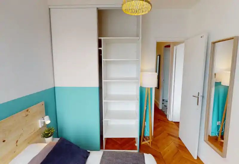 Chambre lumineuse et moderne avec tête de lit en bois, mur d'accent turquoise et penderie ouverte à étagères. Parquet chaleureux et textiles doux pour une ambiance cosy, idéale pour une annonce locative.