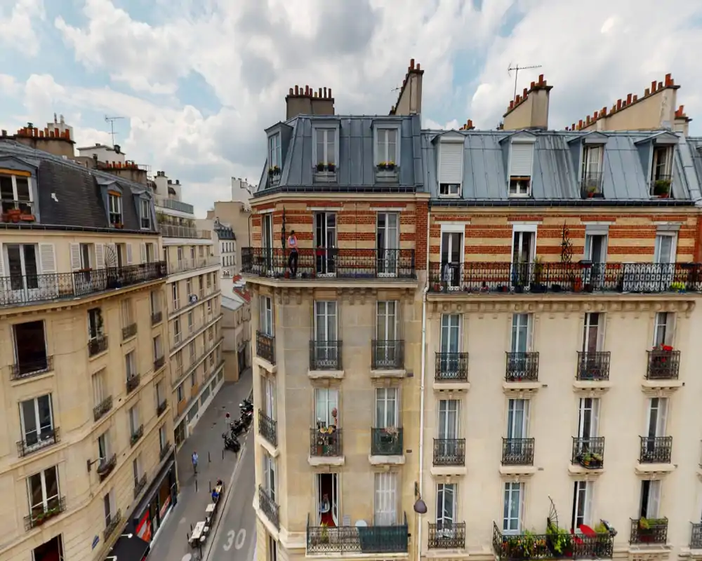 Vue depuis un balcon/terrasse sur des façades parisiennes et la rue en contrebas ; la lumière du jour et les détails architecturaux la rendent appropriée pour une annonce extérieure.
