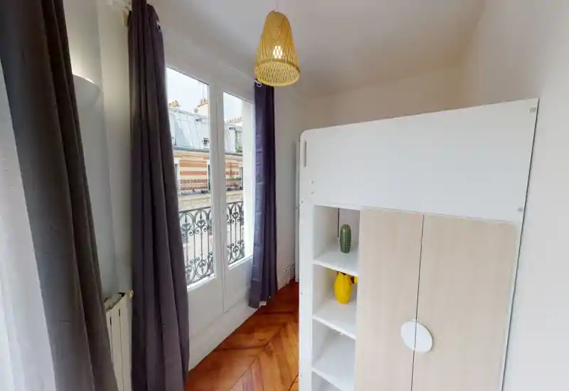 Coin chambre compact avec un lit mezzanine/à étages, lumière naturelle provenant d'une fenêtre-fenêtre et parquet en bois; décoration minimale, espace fonctionnel et lumineux.
