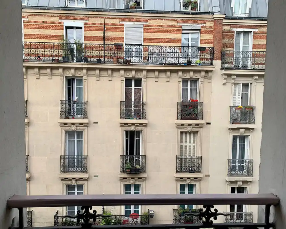 View from a balcony overlooking the façade of a classic Parisian apartment building with decorative wrought-iron railings and window flower boxes.