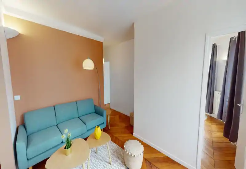 Séjour lumineux et élégant avec un canapé trois places turquoise, parquet en bois, petites tables gigognes et éclairage doux — un espace salon moderne et accueillant.