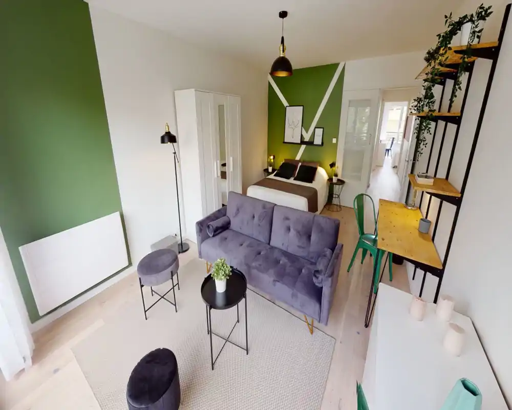 Chambre lumineuse et élégante avec un lit double devant un mur vert accentué, un canapé en velours au premier plan et un petit coin bureau sur le côté. Décoration moderne et chaleureuse, idéale pour une annonce locative.