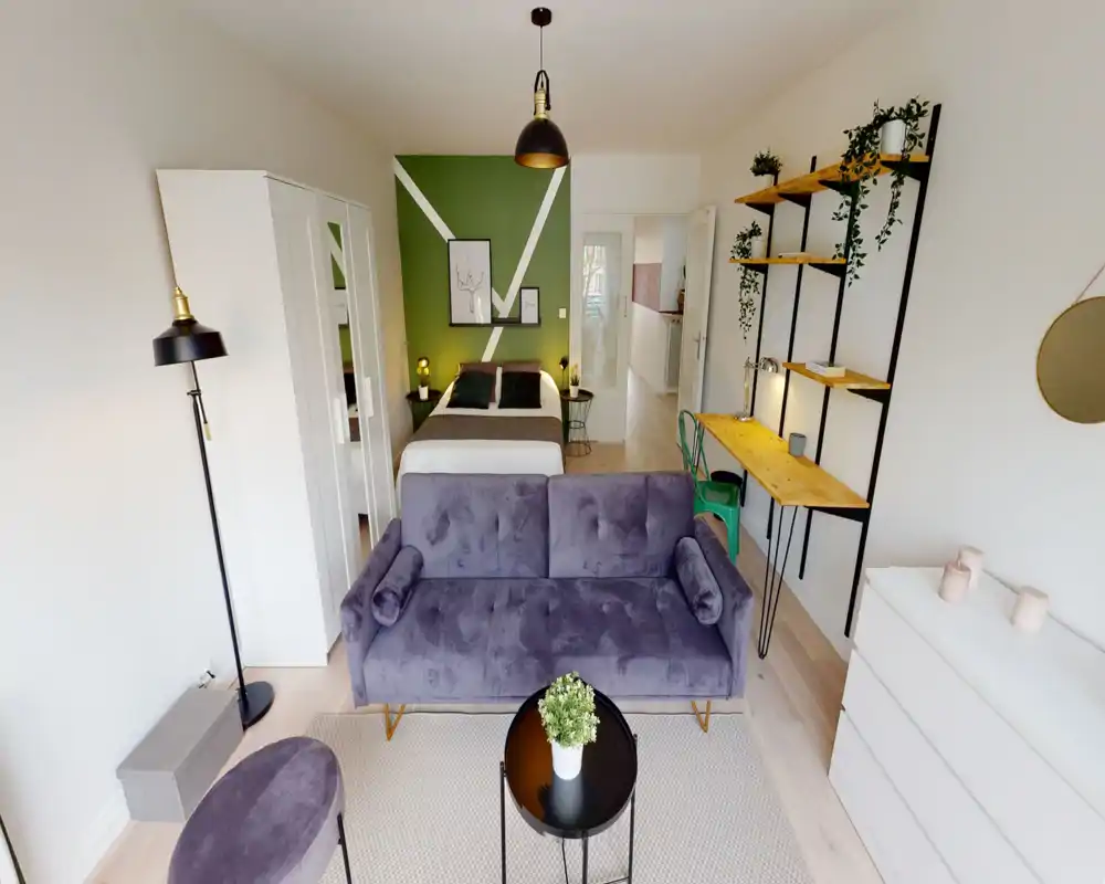 Chambre de style studio lumineuse et moderne avec lit double devant un mur d'accent vert et un canapé en velours face à la caméra ; étagères bureau et plantes décoratives pour un intérieur soigné et convivial.
