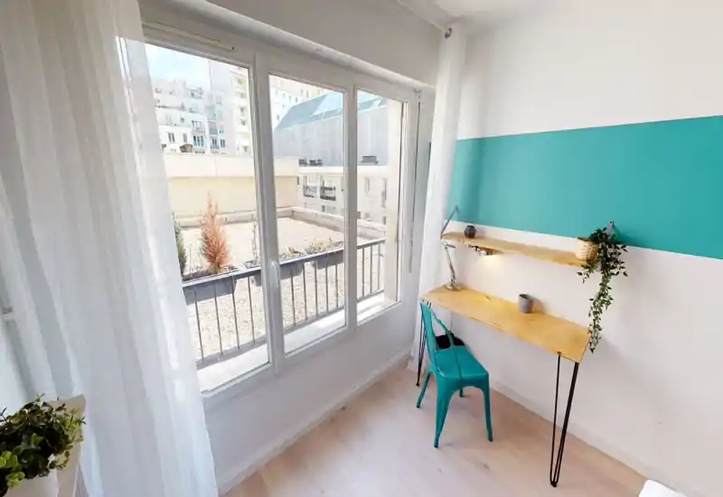 Bright small living/working corner with a large window, wooden wall-mounted desk and teal chair — ideal for a sunny home office or reading nook.