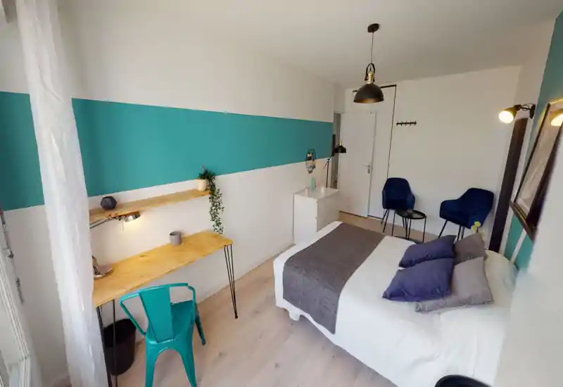 Bright, modern bedroom with a comfortable double bed, coordinated cushions and a neat workspace by the window. Accent teal stripe and matching seating create a stylish, inviting atmosphere ideal for rentals.