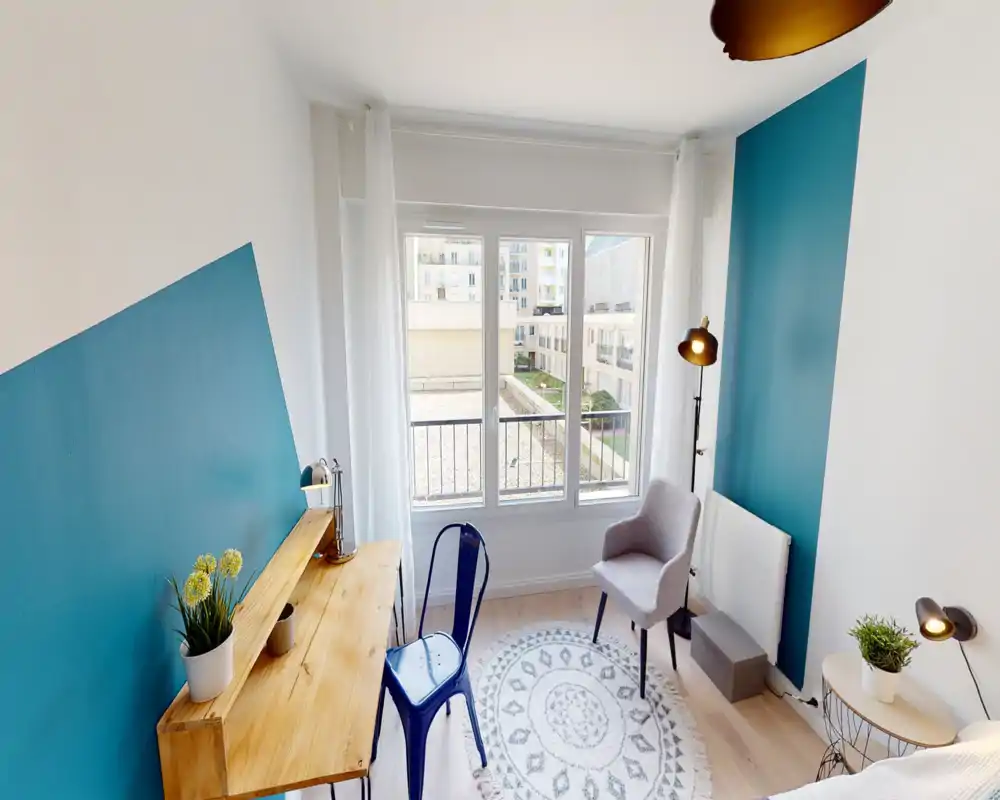 Coin chambre lumineux et moderne avec bureau en bois, murs d'accent bleu canard, fauteuil et grande fenêtre — style soigné et accueillant.