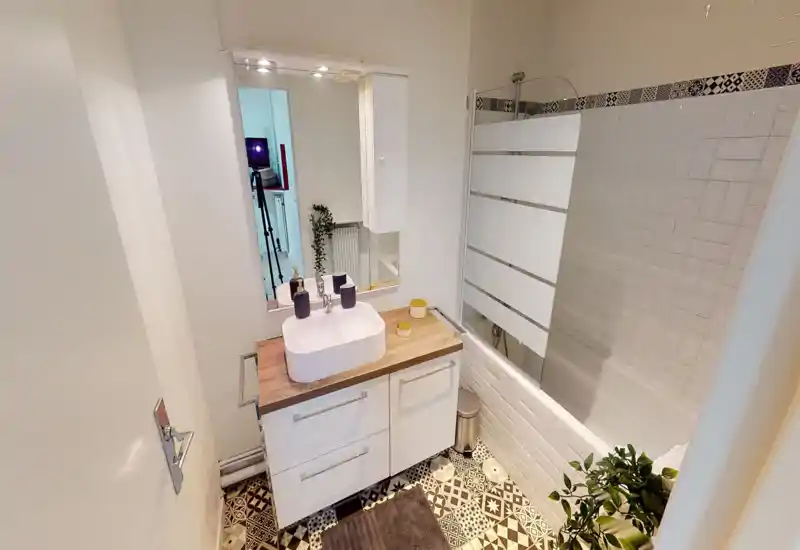 Bright, modern bathroom with patterned floor tiles, a countertop sink on a wood-effect vanity, a mirror cabinet and a bathtub with a glass screen.
