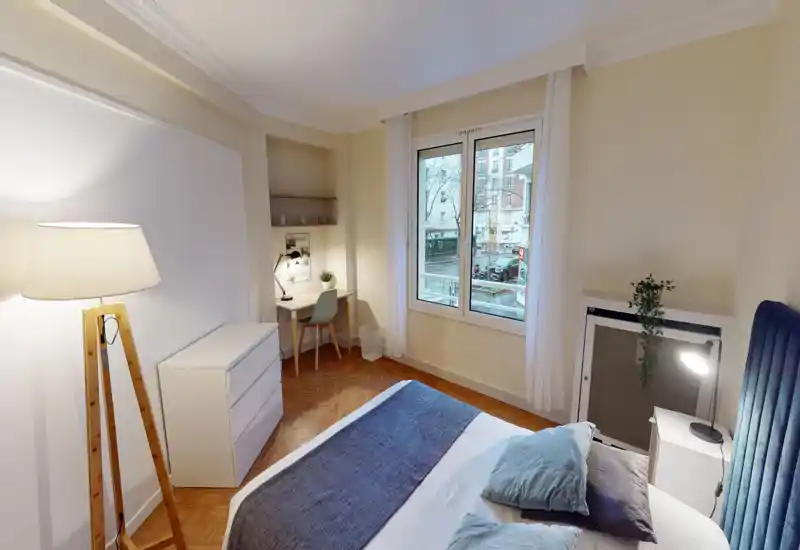 Chambre lumineuse et bien aménagée avec un lit double confortable, une lampe de chevet et un petit bureau près de la fenêtre — idéale pour se reposer et travailler légèrement.