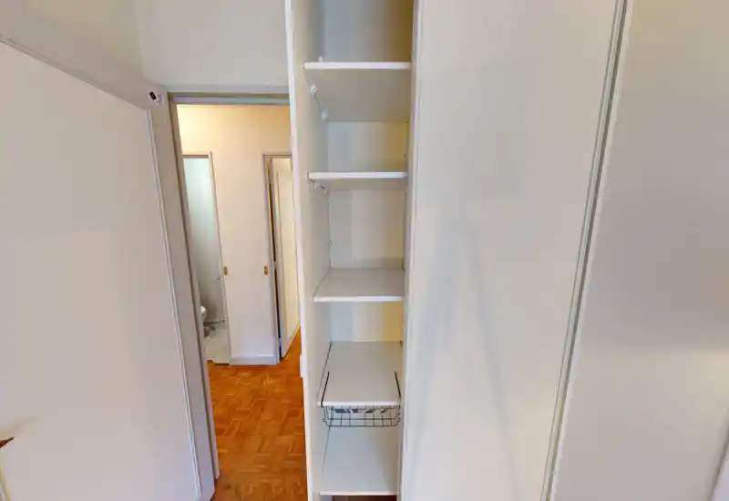 Étagères encastrées étroites et petit couloir/entrée avec parquet ; photo nette montrant les compartiments de rangement et l'accès à la salle de bains adjacente.
