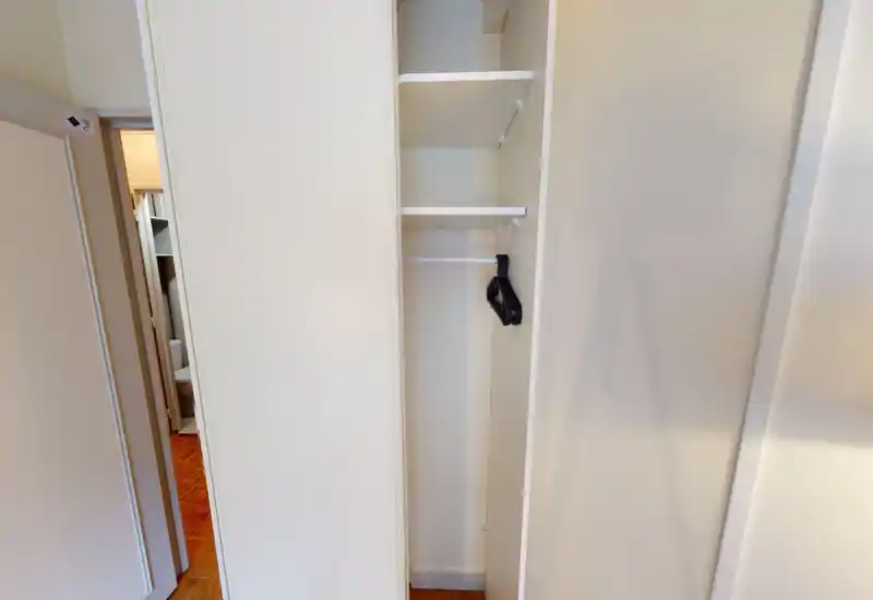 Placard encastré étroit dans un couloir/entrée avec étagères et tringle; quelques cintres vides sont visibles.
