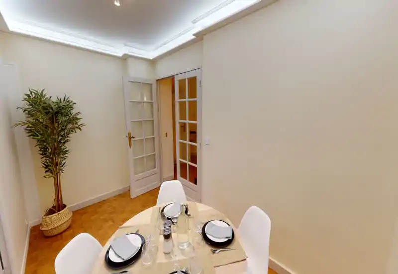 Well-staged dining area with a round wooden table set for four, modern white chairs, and a decorative potted plant creating a warm, inviting atmosphere.