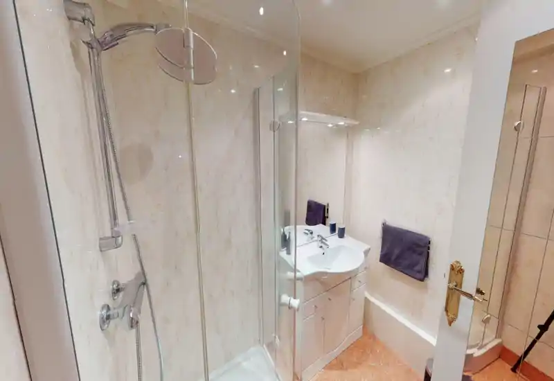 Modern, well-lit bathroom with a glass-enclosed shower, white sink vanity and tiled walls. Clean fixtures and warm floor tiles create a neat, functional space.
