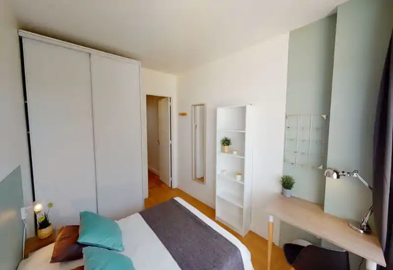 Chambre lumineuse et bien aménagée avec lit double, lampe de chevet, placard et petit bureau près de la fenêtre — idéale pour un séjour confortable ou le télétravail.