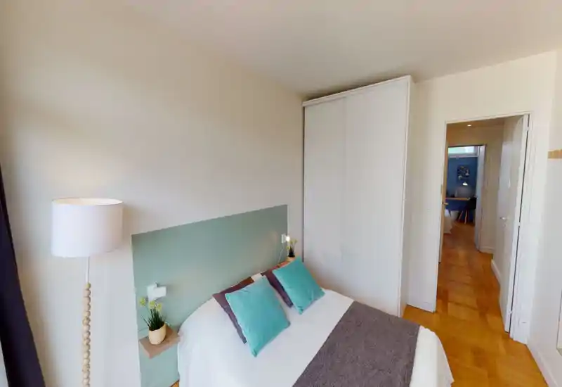 Chambre lumineuse et décorée avec goût, lit double, tête de lit vert turquoise et coussins assortis. Sol en parquet chaleureux, grand placard blanc et éclairage doux pour une atmosphère confortable.